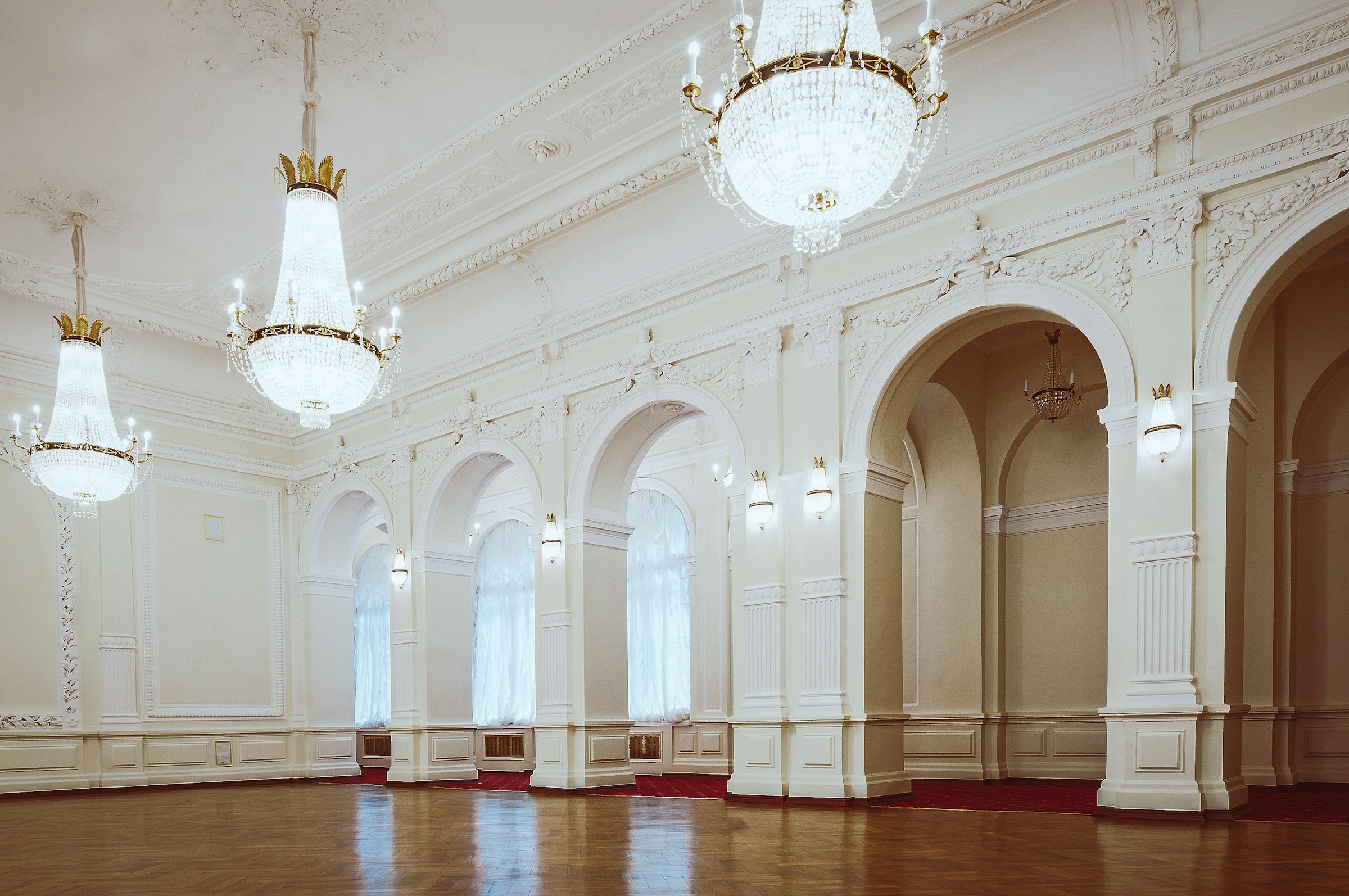 Bright white ballroom with crystal chandeliers and arched windows
